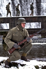 Żołnierz obserwuje teren podczas gdy jego koledzy pokonują rzekę.
