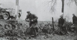 Żołnierze Kampfgruppe Hansen przemieszczają się wzdłuż drogi, na płaszczu pierwszego widoczny orzełek SS na ramieniu.